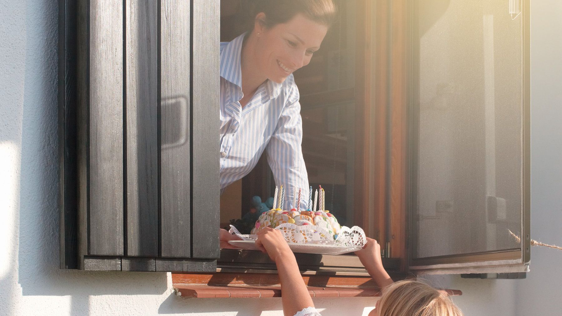 Frau reicht Kuchen durch ein Fenster mit flexiblem Insektenschutz